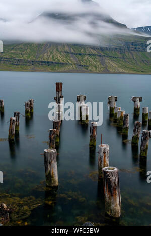 Reydarfjordur Harbour with smooth water and posts in the water on a beautiful sunny summer day in the East of Iceland Stock Photo