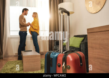 Full-length portrait of young man and woman in casual wear standing near the window in their room in a hotel. They are happy to be together. Travelling together concept. Horizontal shot. Side view Stock Photo