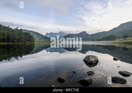 Mirror-like reflections of the Langdale Pikes in Blea Tarn early morning in late summer Stock Photo