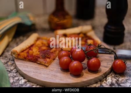 pizza on a cutting board with fresh tomato and oil in a bottle, with pepper in a black wooden pepper mill. Stock Photo
