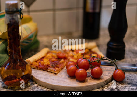 pizza on a cutting board with fresh tomato and oil in a bottle, with pepper in a black wooden pepper mill. Stock Photo