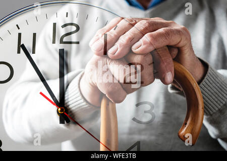 Hands of an elderly man on a cane over a clock dial in a conceptual composite image of memories, passing time and countdown to a deadline Stock Photo