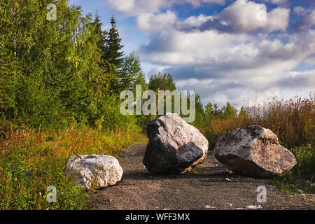 Large boulder stones block the forest road summer landscape. On a forest path is a large rock that blocks the way.
