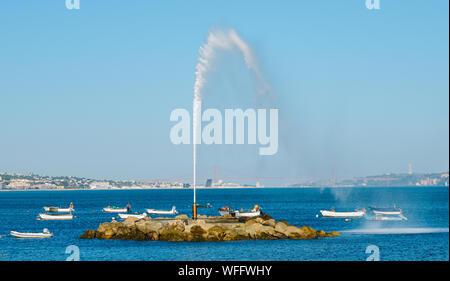 Geyser on River Tagus with fishing boats overlooking 25 April Bridge and Rei Cristo statue in Lisbon, Portugal with copy space Stock Photo