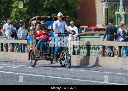 Tourists as passengers on a sightseeing ride in a 3 wheeled Rickshaw or Pedicab across Westminster Bridge in City of London, England, UK. Stock Photo