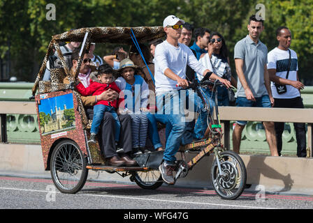 Tourists as passengers on a sightseeing ride in a 3 wheeled Rickshaw or Pedicab across Westminster Bridge in London, England, UK. Stock Photo