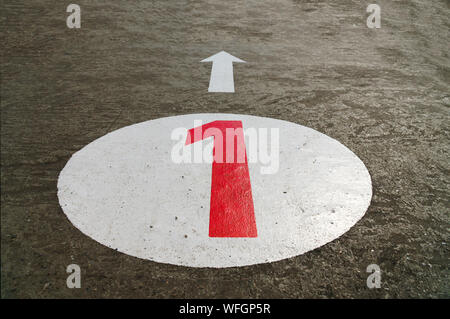 Red number one inside a white circle and an arrow painted on concrete background - 45 degrees angle view, closeup, landscape format Stock Photo