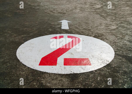 Red number two inside a white circle and an arrow painted on concrete background - 45 degrees angle view, closeup, landscape format Stock Photo