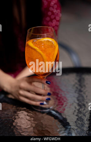 Woman sitting at a table holding an aperol spritz cocktail Stock Photo