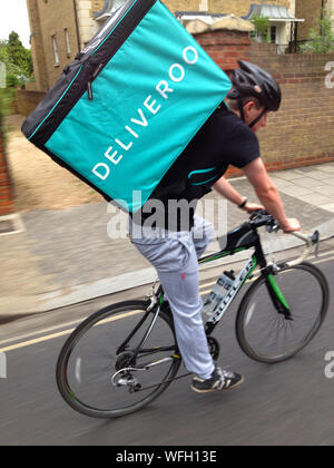 Deliveroo take away / takeaway food / meal delivery cyclist / rider pedalling hard with an insulated backpack on his back to deliver a meal to someone's house, home or office. Richmond-upon-Thames, London. UK (stomo) Stock Photo