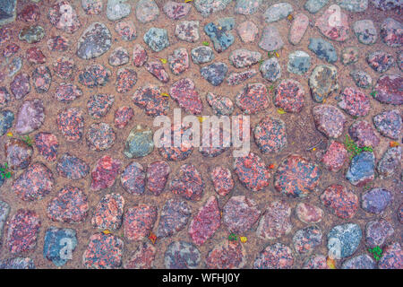 Stone background of pavement with rough wet granite boulders. Texture of historic medieval cobble paving is laid on the city street Stock Photo