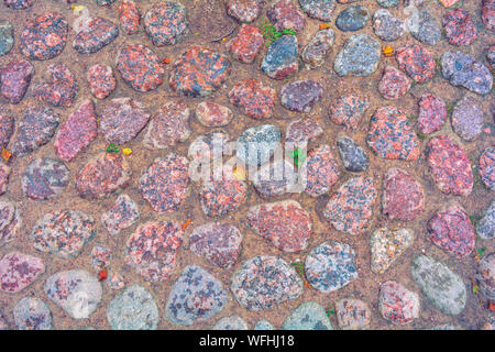 Stone background of pavement with rough wet granite boulders. Texture of historic medieval cobble paving is laid on the city street Stock Photo