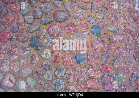 Stone background of pavement with rough wet granite boulders. Texture of historic medieval cobble paving is laid on the city street Stock Photo
