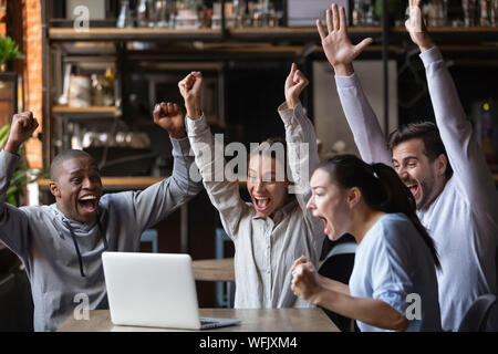 Euphoric diverse friends celebrating victory watching online game on laptop Stock Photo