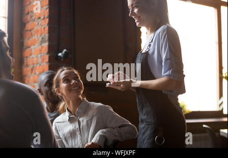Happy waitress holding notepad taking order serving clients in cafe