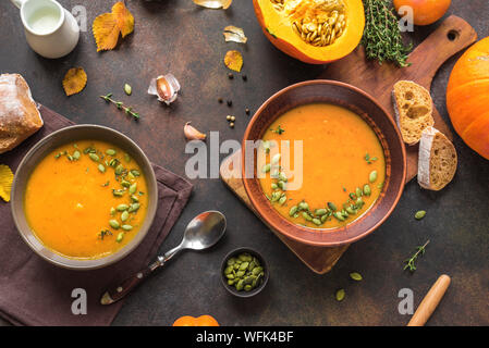 Pumpkin soup and organic pumpkins on rustic wooden table. Seasonal autumn food - Spicy pumpkin soup with thyme and pumpkin seeds. Stock Photo