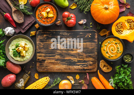 Autumn soups. Set of various seasonal vegetable soups and organic ingredients on dark background, top view, copy space. Homemade colourful vegan soups Stock Photo