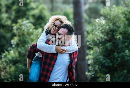 Cheerful couple of beautiful adult people have fun together in outdoor leisure activity in the wood - nature green forest in background - concept of h Stock Photo
