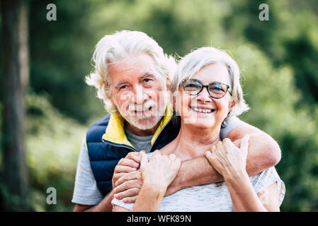 People in love at old age - couple of caucasian cheerful happy senior smile and hug in relationship - green defocused forest in background for outdoor Stock Photo