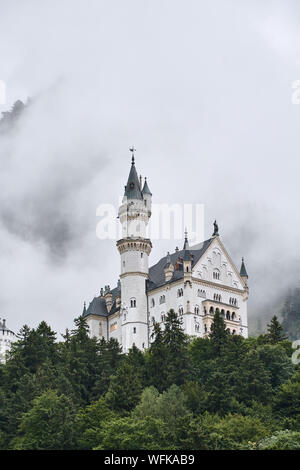 Neuschwanstein Castle (Schloss Neuschwanstein) from the town below, surrounded by fog and trees - in Schwangau, Germany Stock Photo