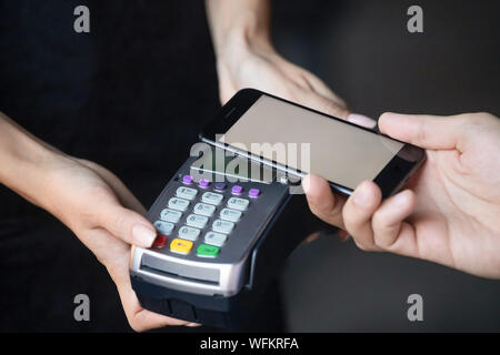 Male customer make payment holding phone above nfc terminal, closeup Stock Photo