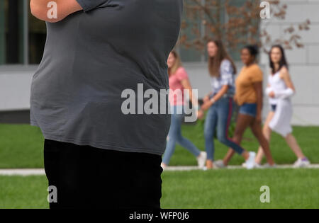 An obese individual being looked upon by a group of young women. Obesity is a national epidemic affecting an alarming amount of our population. Stock Photo