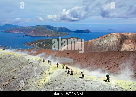 Italy, Sicily, Aeolian Islands, listed as World Heritage by UNESCO, Vulcano Island, hikers at the edge of the crater of volcano della Fossa walking through sulfur fumaroles, Lipari Island in the background on the left and Panarea then Stromboli on the right (aerial view) Stock Photo