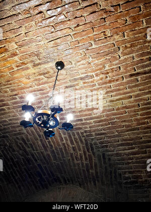 Antique chandelier style with modern lights. It hangs on a red brick ceiling. Rusty look picture. Stock Photo