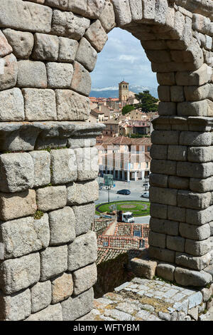 SEGOVIA, SPAIN - APRIL 25, 2018: View through one of the arches of the Roman Aqueduct with the Artillery Square and the tower of El Salvador church. Stock Photo