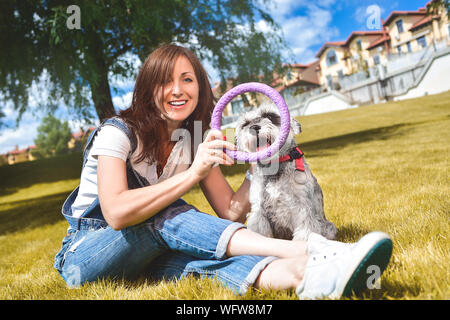 Caucasian joyful woman playing with her beloved dog in the park. The concept of love for animals. best friends. Dog breed Schnauzer Stock Photo