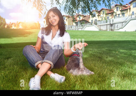 Caucasian joyful woman playing with her beloved dog in the park. The concept of love for animals. best friends. Dog breed Schnauzer Stock Photo