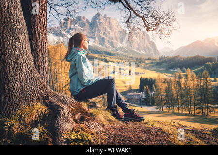 Woman is sitting on the hill under the tree at sunset in autumn Stock Photo