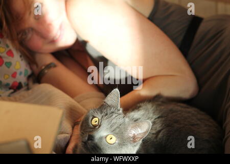 Close-up Portrait Of Cat Relaxing On Bed With Woman At Home