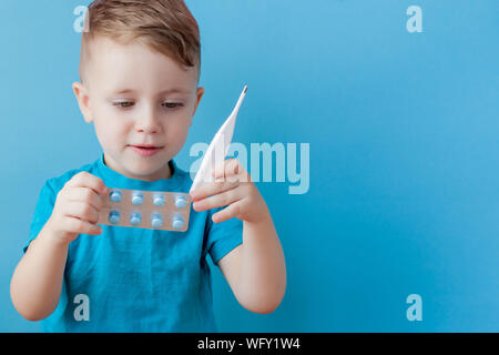 Ill young child with a thermomether, measuring the height of his fever and looking into the camera Stock Photo