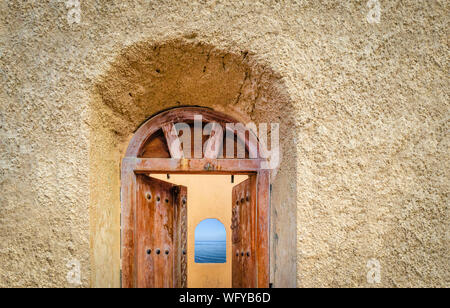 Old, antique door of a watchtower opening to reveal a arch window to the sea. From Muscat, Oman. Stock Photo