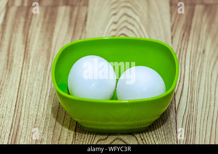 Two eggs in a green bowl on a wooden table Stock Photo