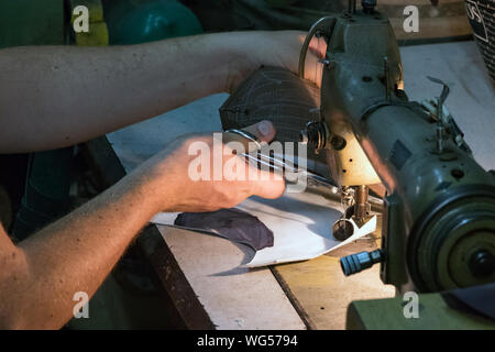 A male shoemaker cutting a thread after sewing leather with an old sewing machine. Stock Photo