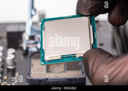 hand in black glove installing central processor unit in pc motherboard - closeup with selective focus and blur Stock Photo