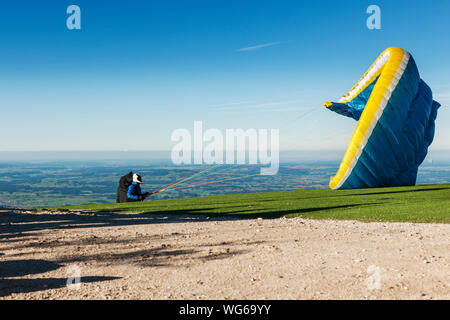 A paraglider at the take-off point on the Tegelberg in Bavaria unfolds his paraglider as the last preparation before the jump. Stock Photo