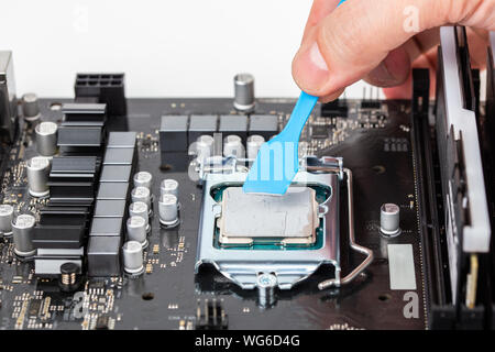 hand applies gray thermal grease on central processor unit in pc motherboard - closeup with selective focus and blur Stock Photo