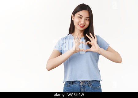 Girl confess true feelings love girlfriend. Tender cute brunette asian woman show heart gesture tilt head smiling silly romantic cheerful mood happy Stock Photo