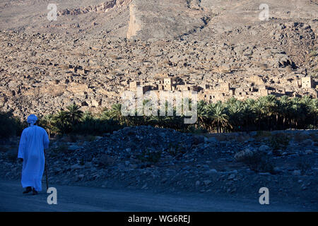 Man in traditional clothes walking in shadow to the abandoned Village near Nizwa - Oman, Ghool village at the start of Wadi Nakhr Stock Photo