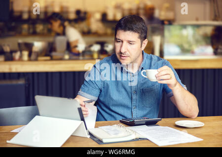 Successful new business owner calculating bills and expenses using digital tablet Stock Photo