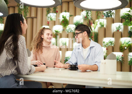Multi-ethnic group of three college students in cafe, chatting while enjoying lunch together and discussing studying, copy space Stock Photo