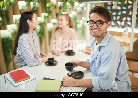Multi-ethnic group of students studying together in cafe, focus on mixed-race young man smiling at camera, copy space Stock Photo