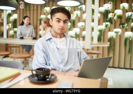 Portrait of mixed race college student using laptop in cafe and looking at camera, copy space Stock Photo