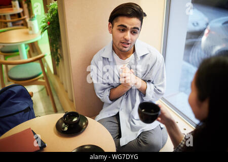 High angle portrait of young couple talking in coffee sitting by window table, focus on mixed-race man, copy space Stock Photo
