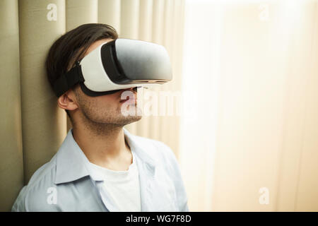 Head and shoulders portrait of man wearing VR helmet leaning against wall in empty room, copy space Stock Photo
