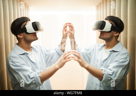 Side view mirror image of young man wearing VR helmet interacting with reflection, copy space Stock Photo