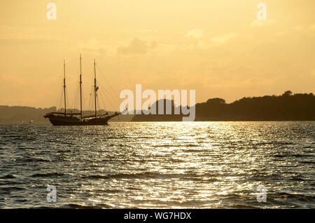 Old sail ship drifts to port seen as a silhouette in backlight. Stock Photo